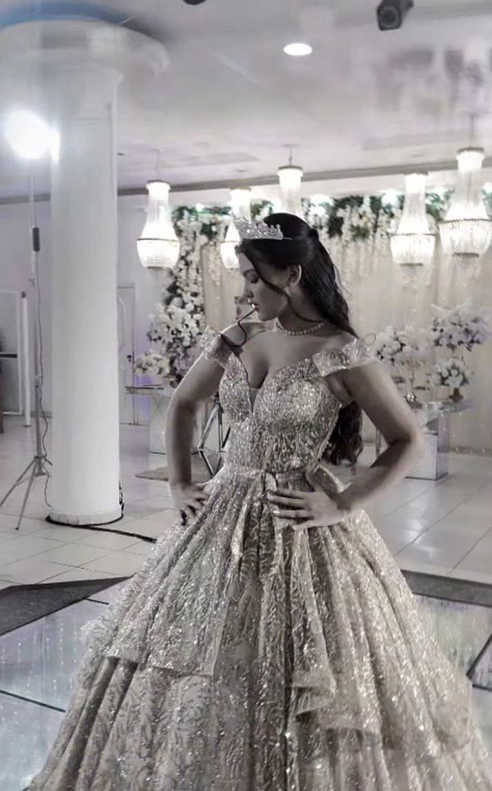 Debutante de coroa e vestido prateado no salão do Estrela Buffet, entre lustres e arranjos de flores brancas