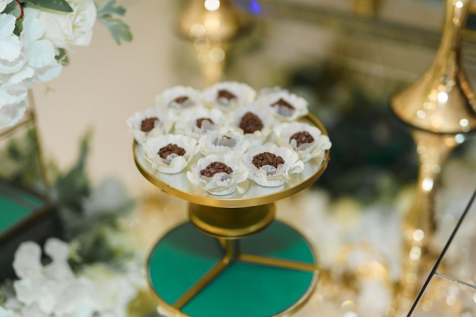 Doces finos dispostos em prato dourado na mesa de doces