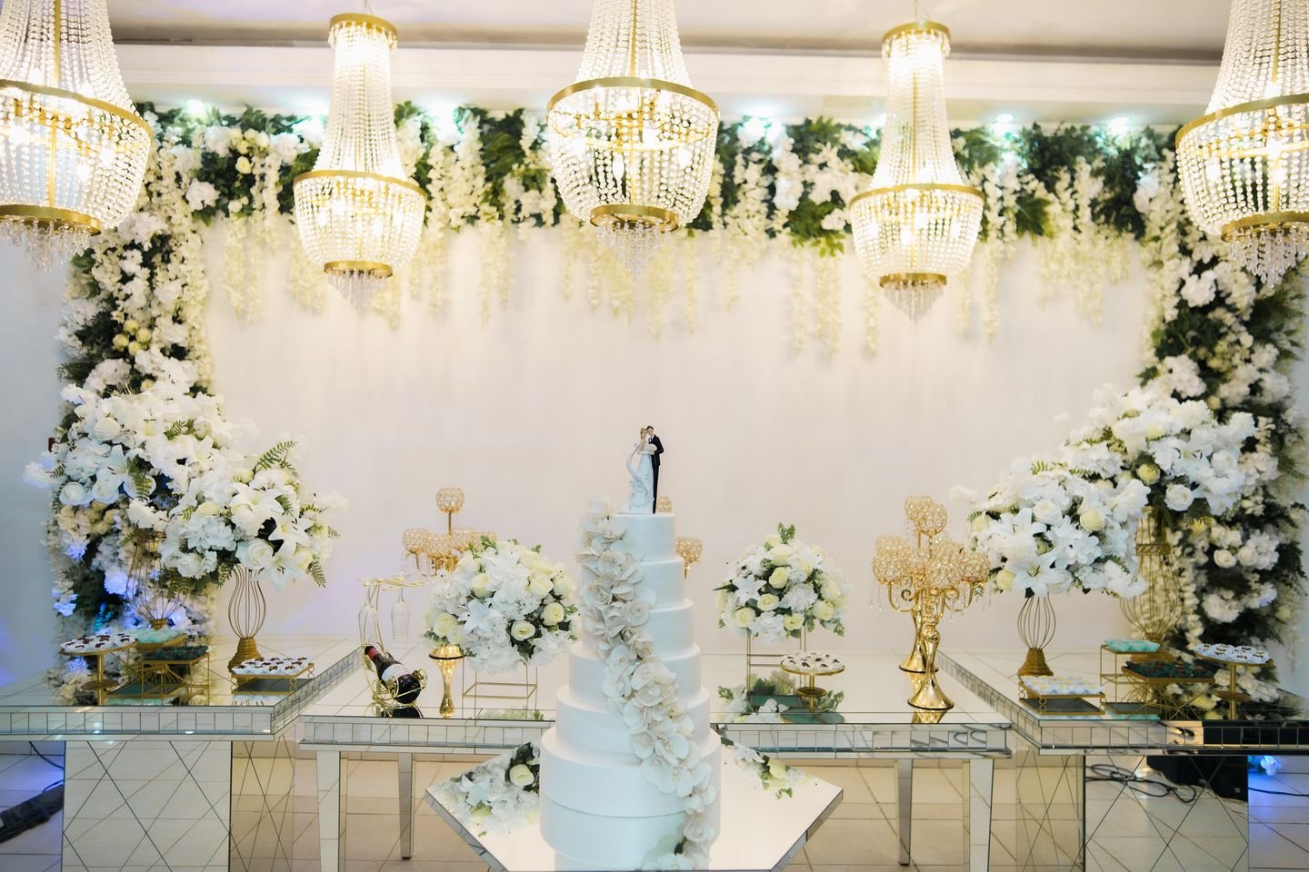Mesa do bolo do Estrela Buffet com arranjos de flores brancas e lustres de cristal