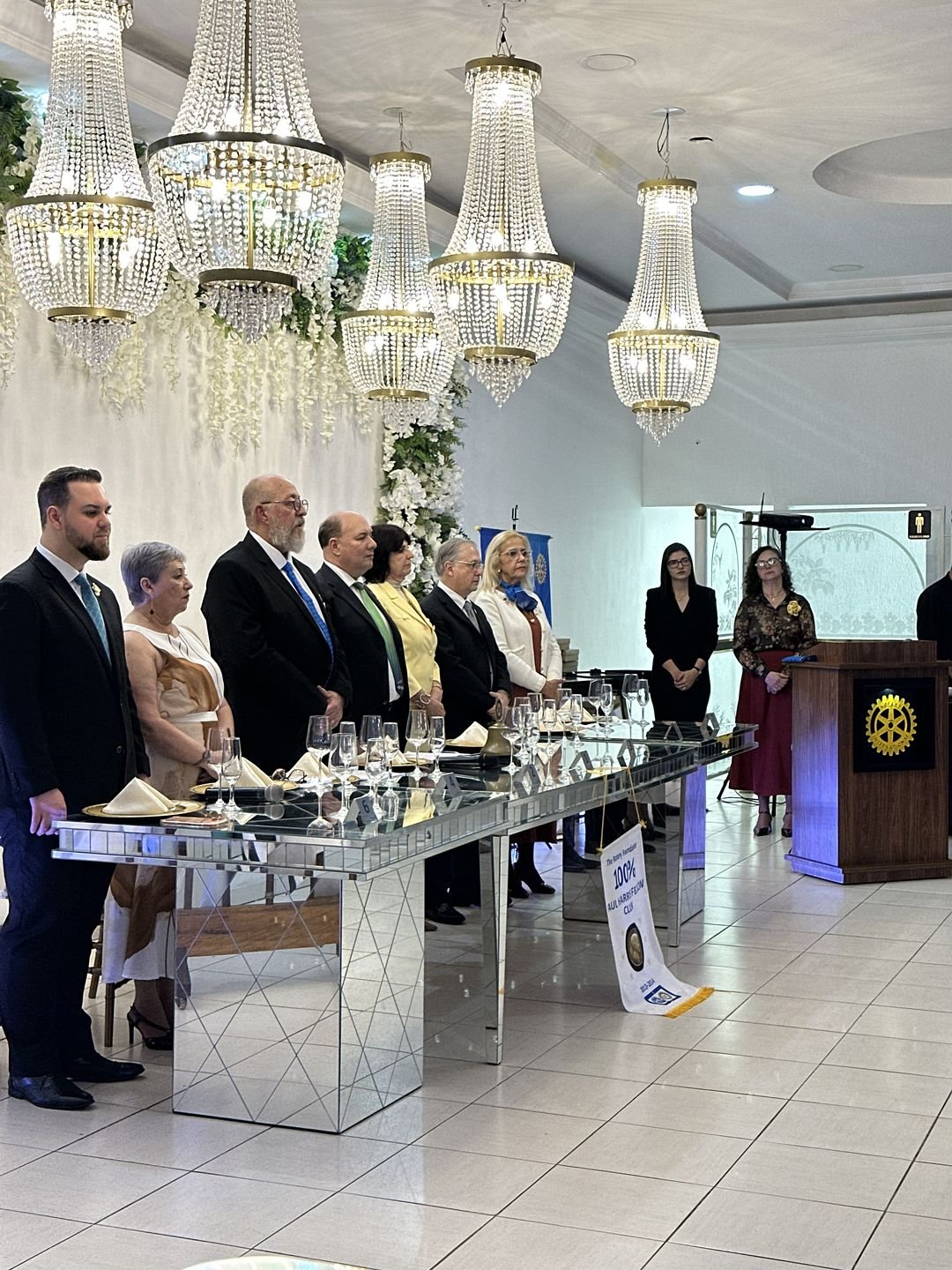 Participantes reunidos em pé junto à mesa imperial durante cerimônia no Estrela Buffet